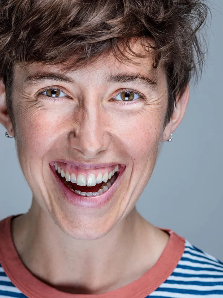 An image of Claire Parry smiling gleefully in a blue and white striped top. White woman with short brown hair and brown eyes. 