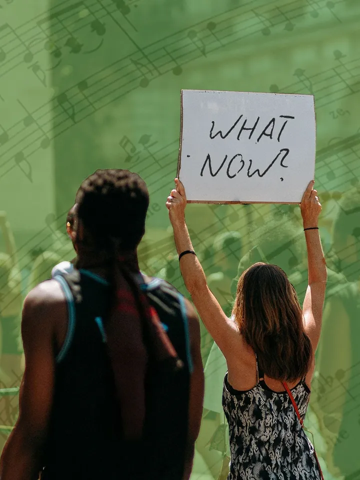 A person holds a sign reading "WHAT NOW?"
