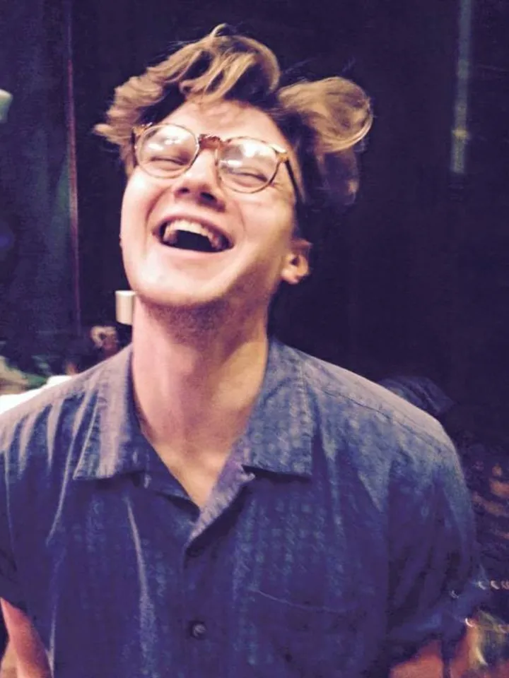Casting Director, Jacob Sparrow, laughing. Dressed in a blue shirt, with spectacles and mid-length brown hair.