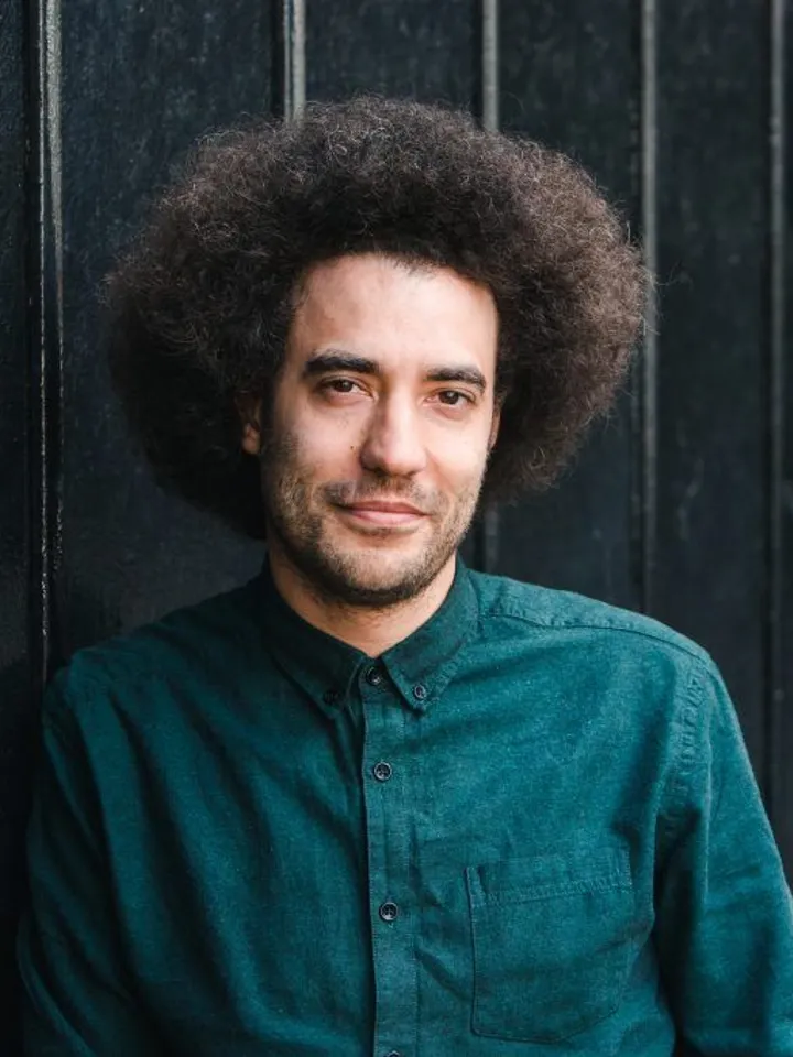 Justin Audibert's headshot, stood in front of black grates with a dark green shirt on.