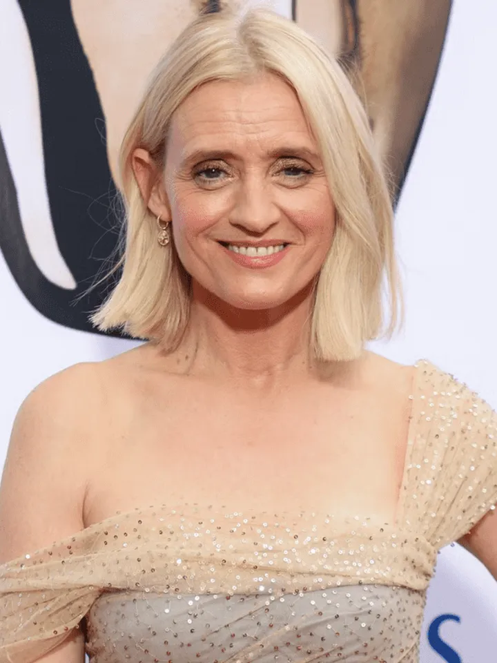 Anne-Marie Duff at the BAFTAs. wearing a sparkly champagne coloured dress. Anne-Marie is a white Irish woman who has blonde hair in a bob, with a gold earring and has a teeth showing smile.