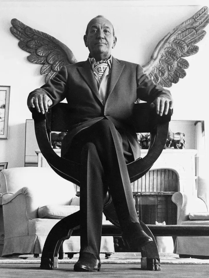 Noel Coward - 1963, sat on chair with wings behind him