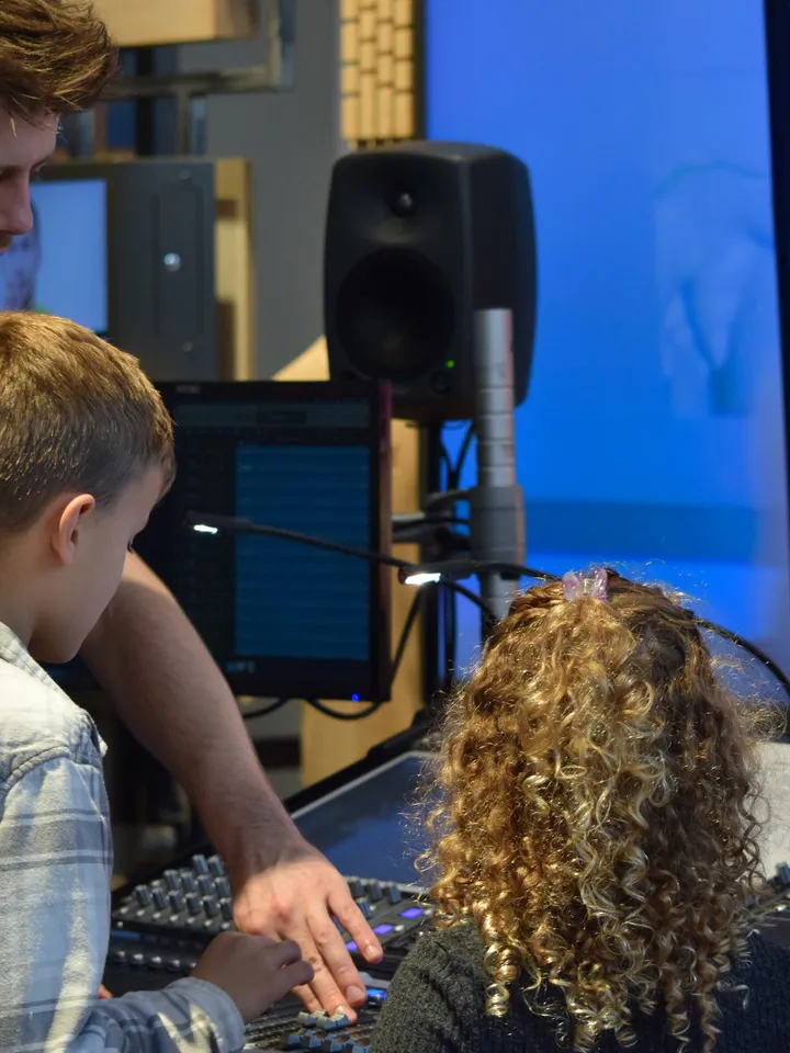 A theatre professional shows two children how to operate a board