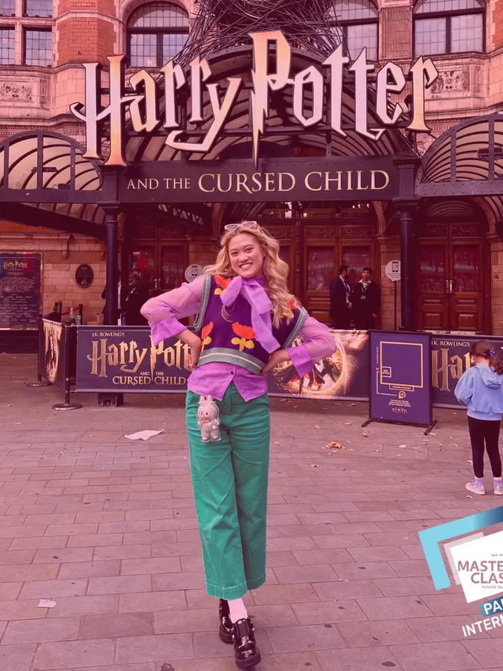 A young woman standing in front the Palace Theatre, dressed in purple and green