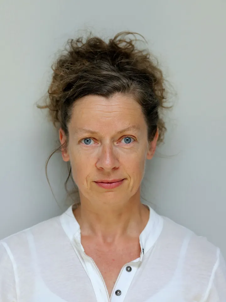 Sinéad Rushe Headshot - White woman with blue eyes and brown hair wearing a white top against a pale background.